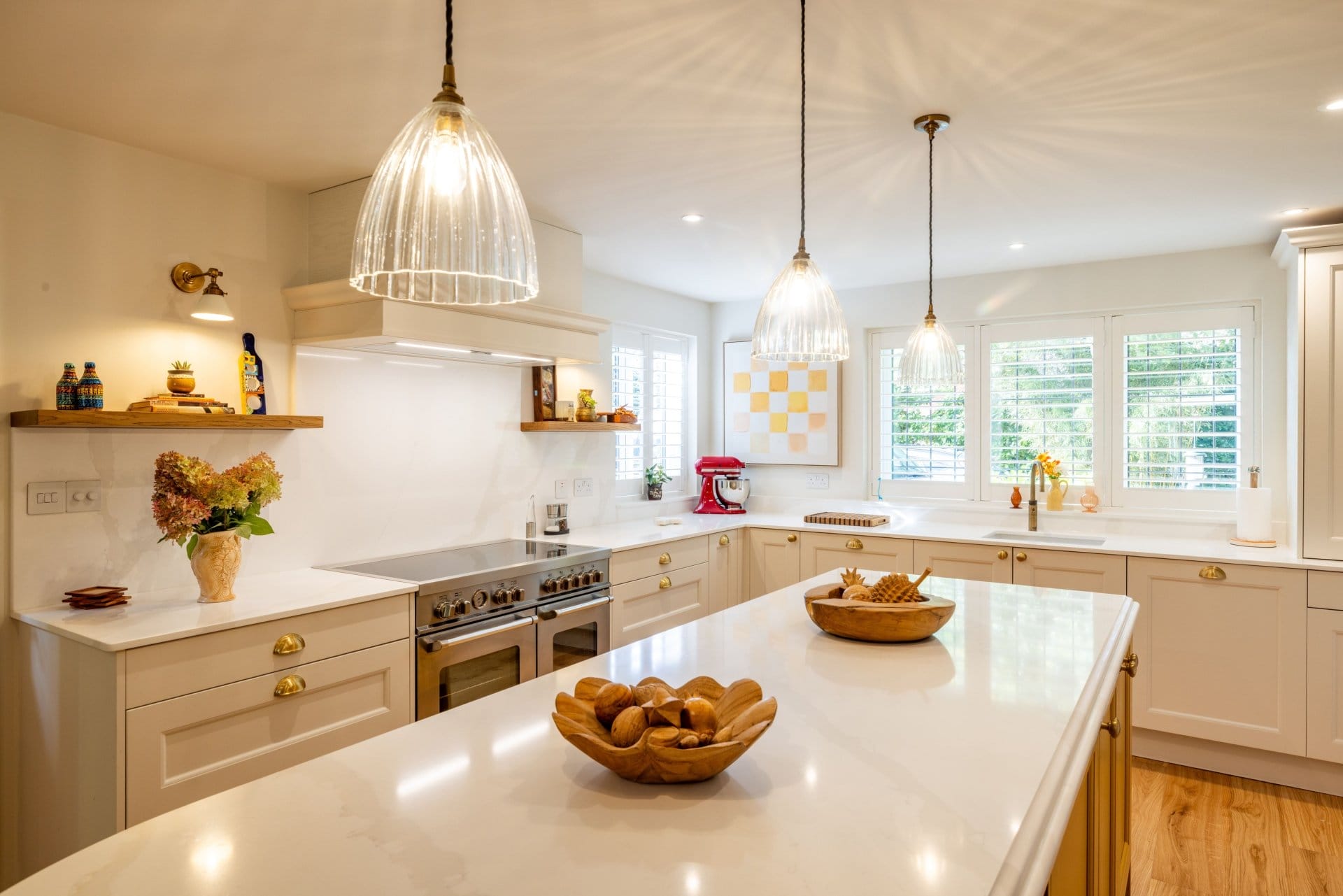 Artizan Interiors bespoke shaker kitchen featuring a large white island, quartz worktops, brass handles, pendant lighting and warm wooden flooring.