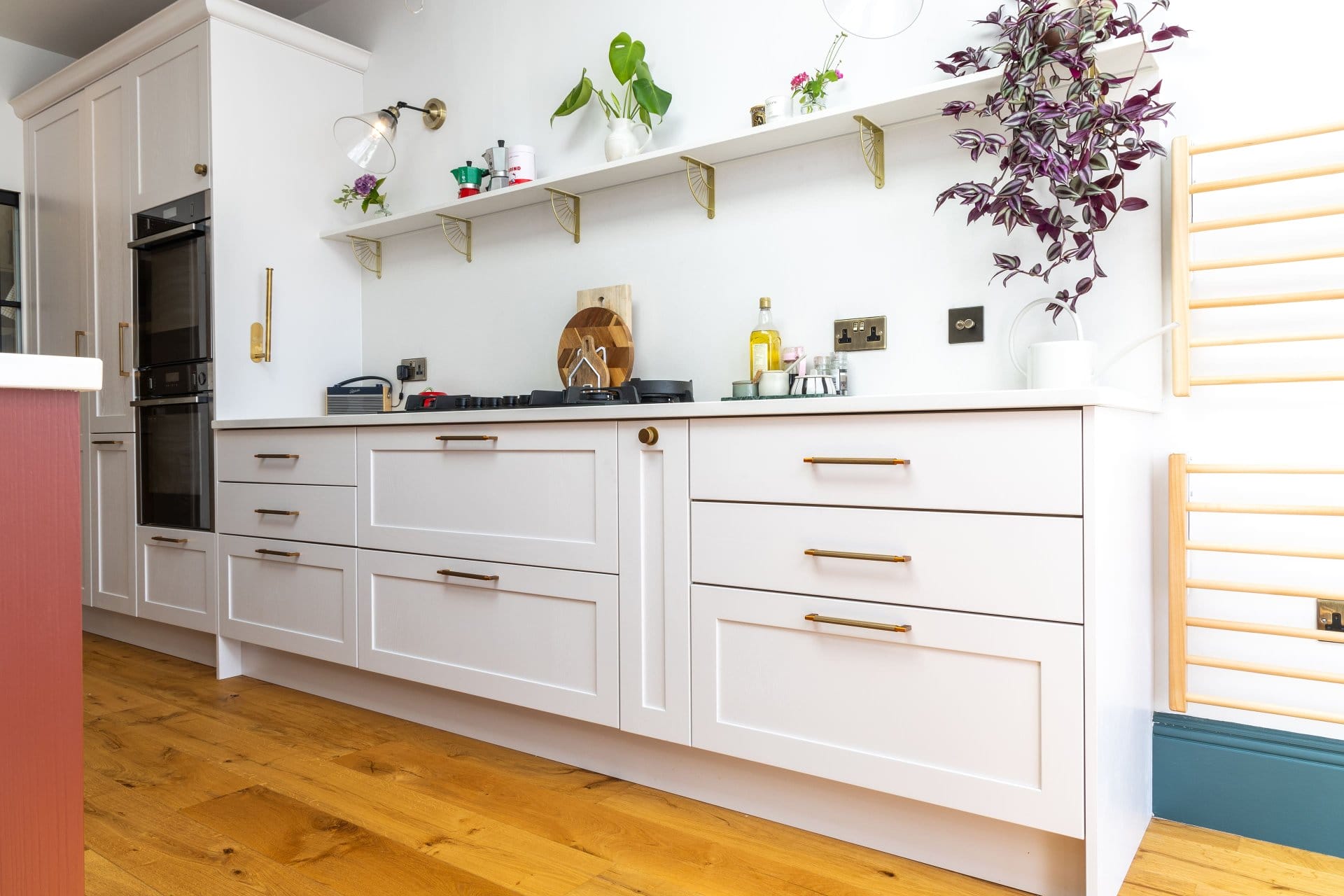 Artizan Interiors bespoke shaker kitchen cabinetry featuring white drawers with brass handles, floating shelves, oak flooring and contemporary styling details.