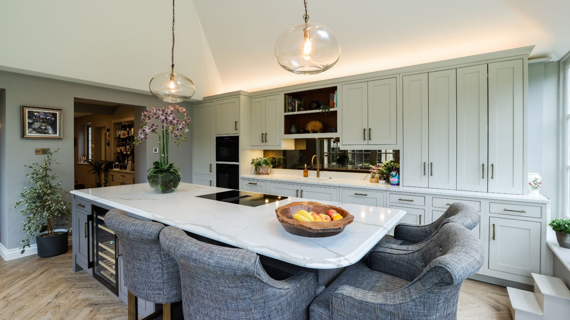 Artizan Interiors luxury shaker kitchen featuring a large marble waterfall island, upholstered breakfast bar seating, bespoke cabinetry and soft contemporary lighting.