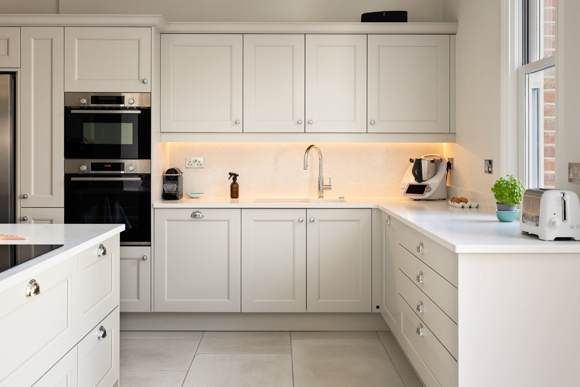 Bright contemporary shaker kitchen with cream cabinetry, integrated appliances, quartz worktops and soft under-cabinet lighting.